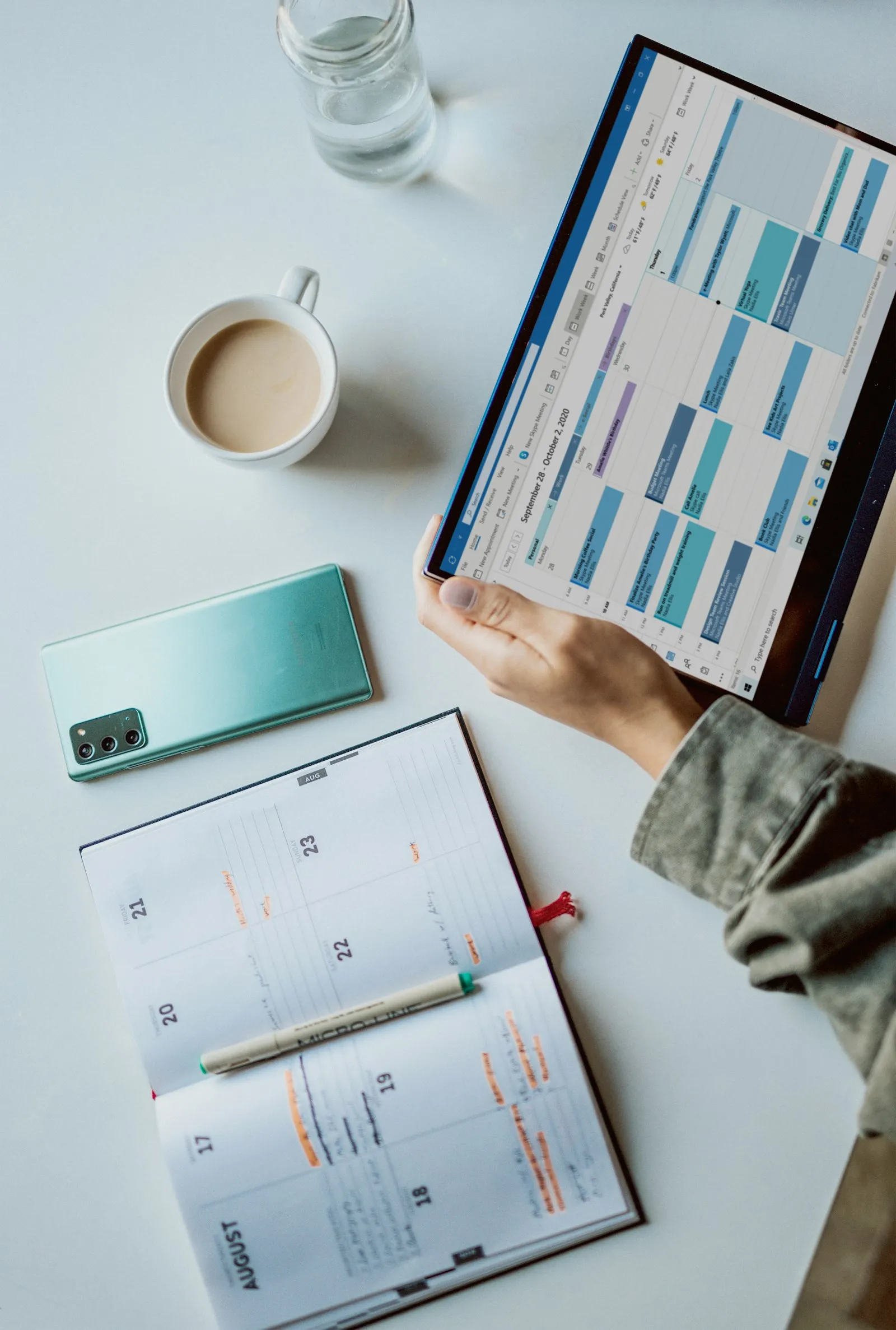 Agenda en ligne affiché sur une tablette, à côté d’un téléphone et d’un agenda papier